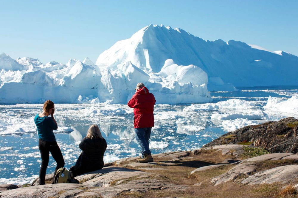 people taking pictures of an iceberg in greenland