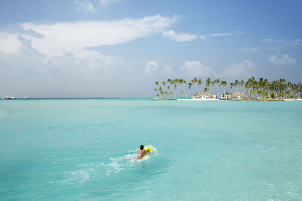 person swimming in clear blue water at Cheval Blanc Randheli resort in the Maldives
