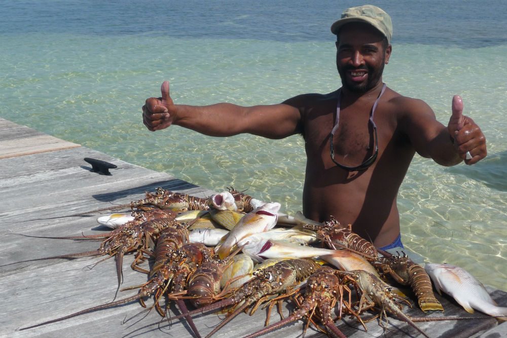 Belize fisherman showing off his fishing catch on a dock, giving two thumbs up