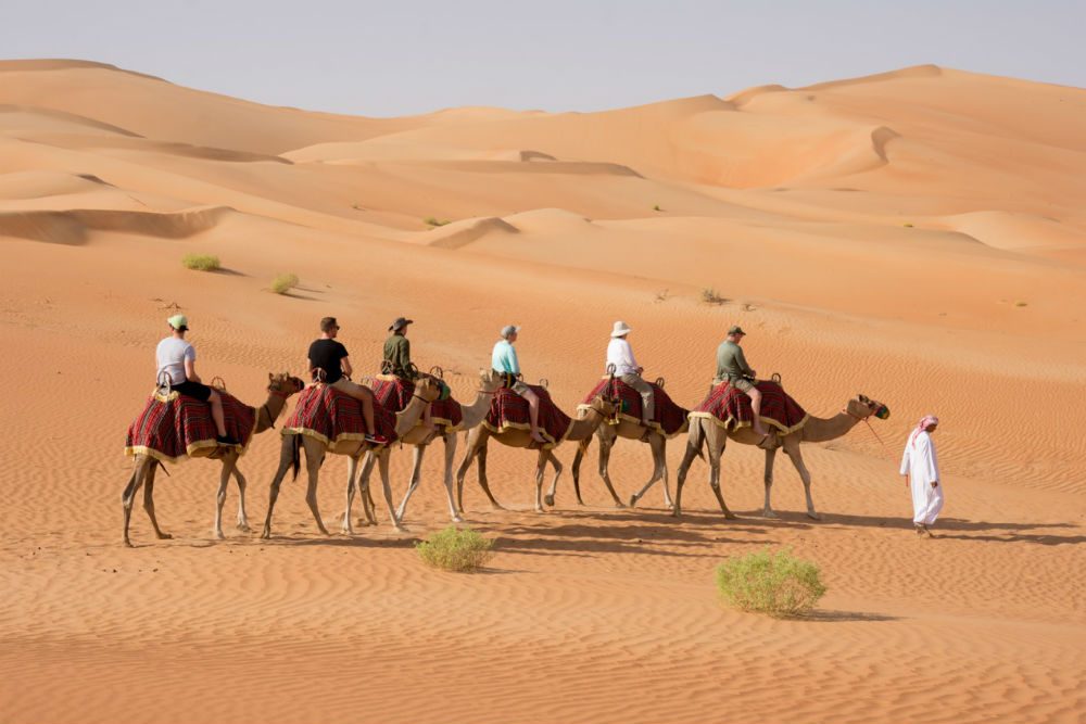 family riding camels in desert in UAE
