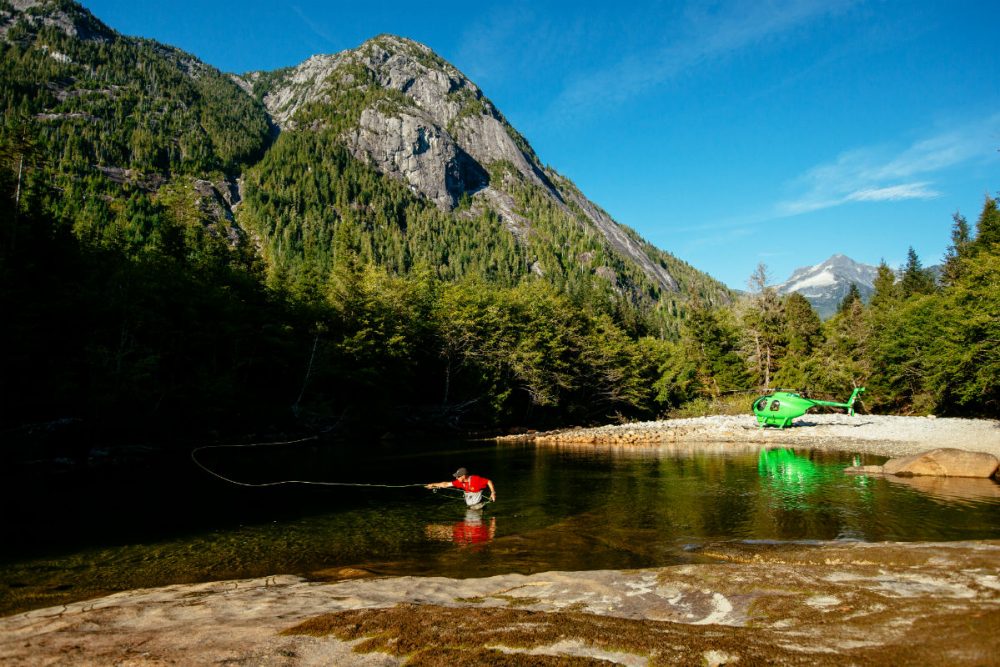 fisherman in a river with a helicopter parked nearby in the mountains of British Columbia Canada