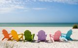 Colorful empty adirondack Chairs lined up on a sunny Beach