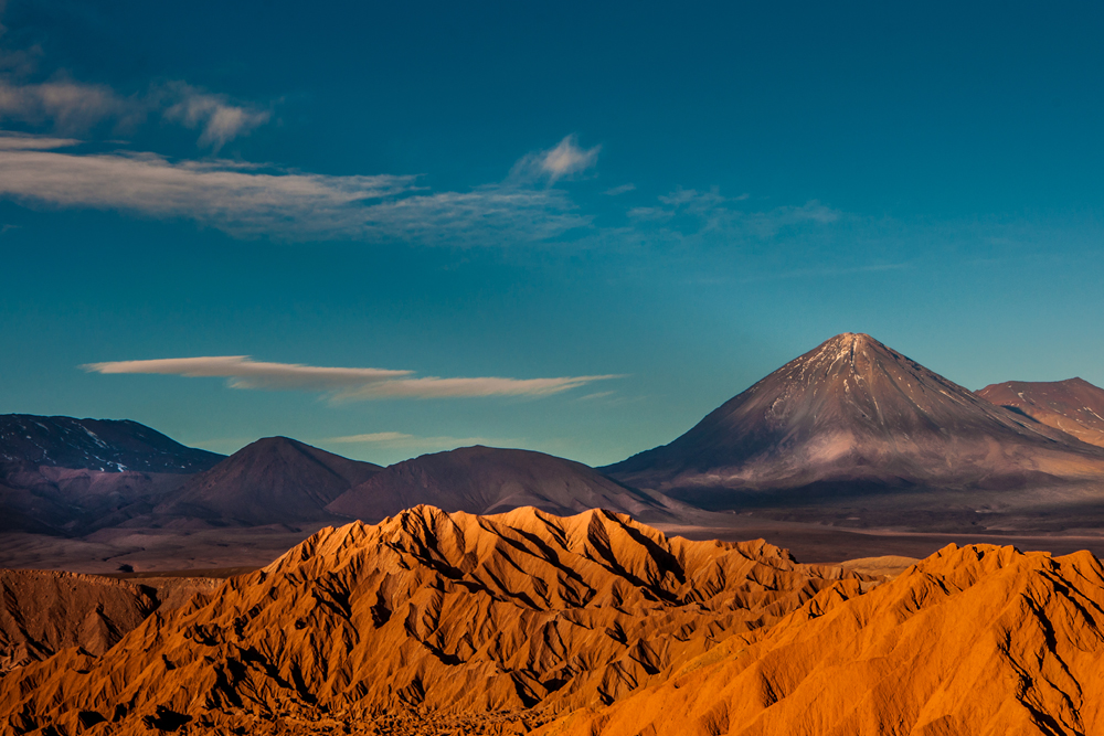 the red sand of Chile's Atacama desert with tall mountains in the distance