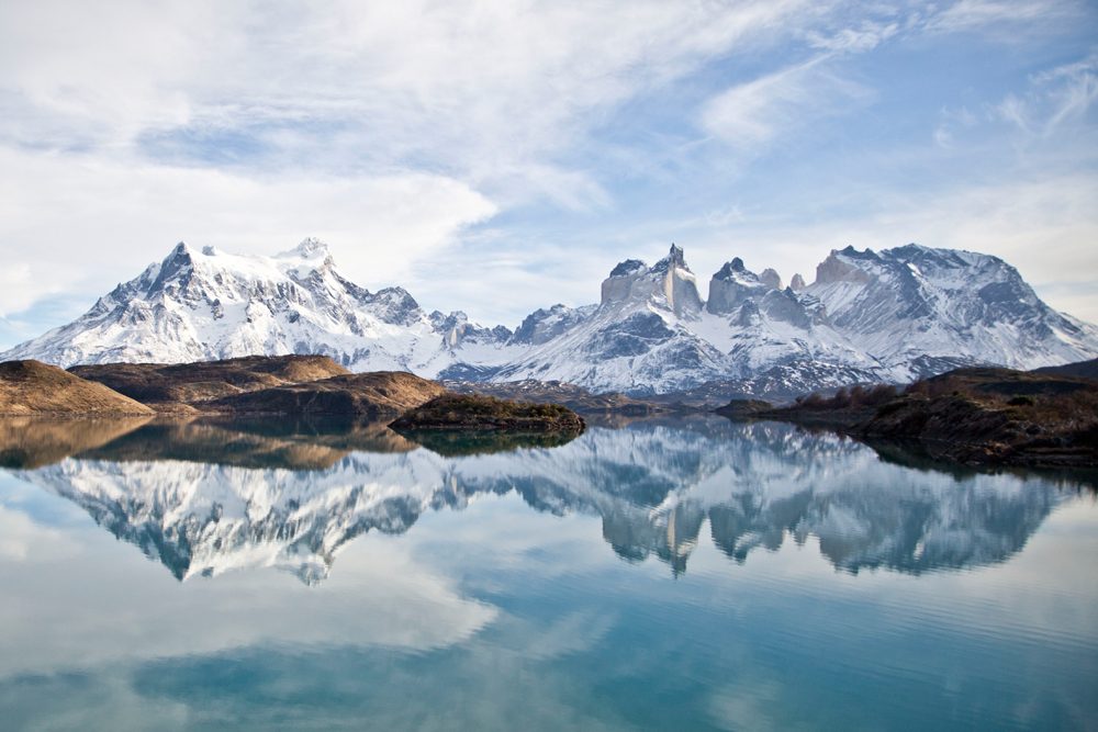 snowy mountains reflect perfectly in a blue lake in Torres del Paine park in Patagonia