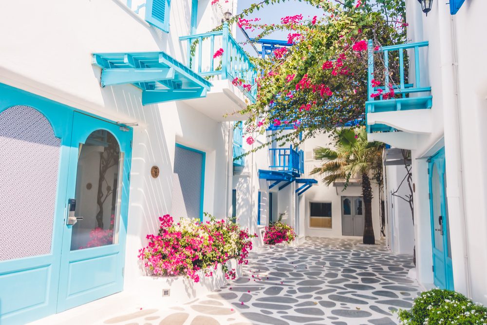 A village street of Santorini is bright white and blue, with pops of pink bougainvillea flowers