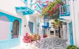 A village street of Santorini is bright white and blue, with pops of pink bougainvillea flowers