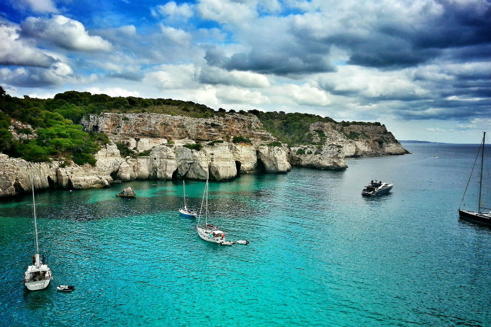 sailboats moored in turquoise water off a rocky shore in Menorca Spain