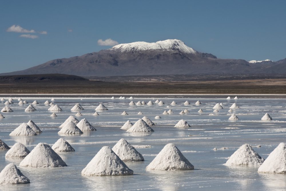 small piles of sand dot the Salar de Uyuni salt flat in Bolivia. A snowy mountaintop is in the background