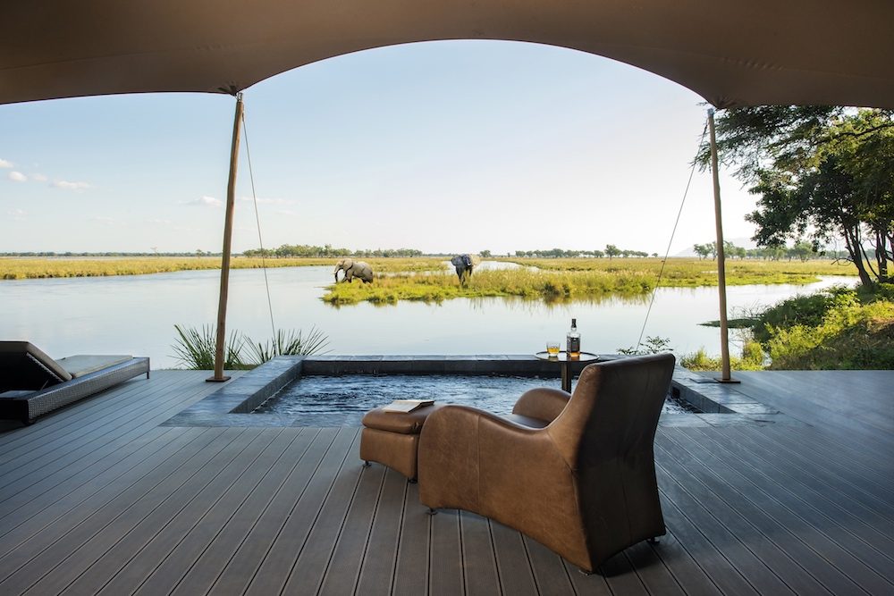 Lounge chair at Sausage Tree Safari camp in Zambia overlooking pool and watering hole and elephants on safari