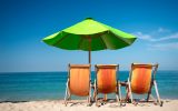 three orange beach chairs and a green umbrella facing the ocean in Puerto Vallarta Mexico