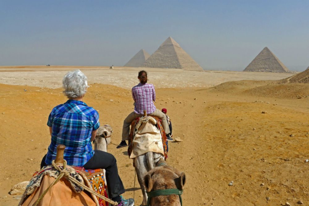 two tourists Riding camels to the pyramids in Egypt
