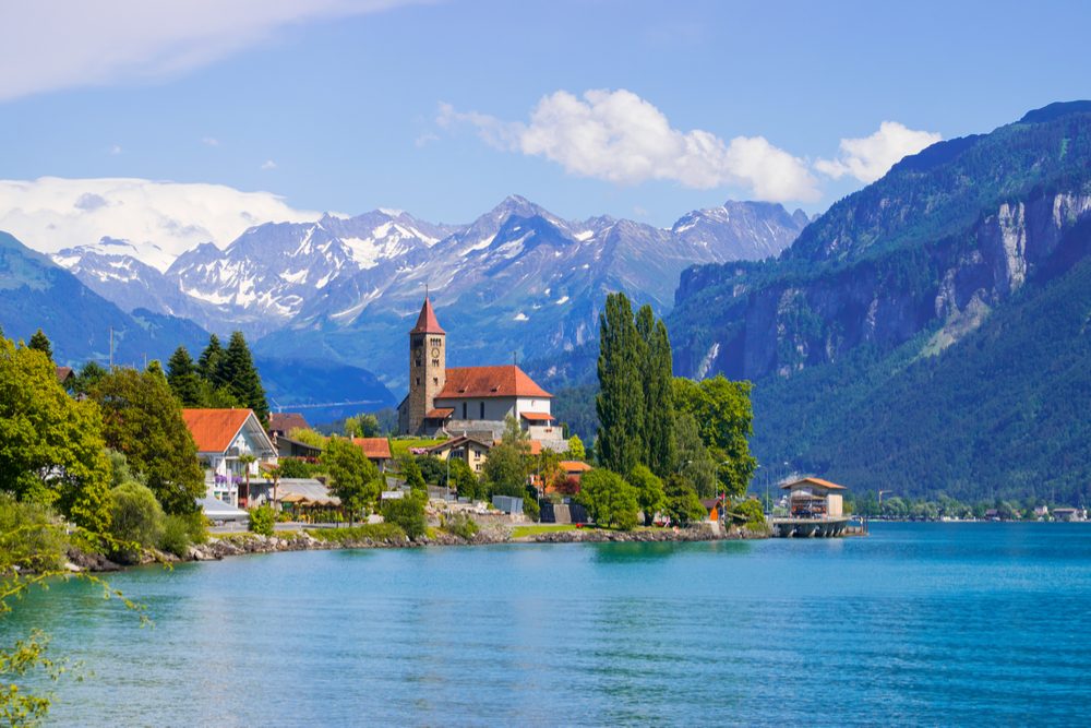 Panoramic view to the Brienz town on lake Brienz by Interlaken, Switzerland. Old fishing town with beautiful church and snow covered Alps mountains on background. Switzerland, Europe.