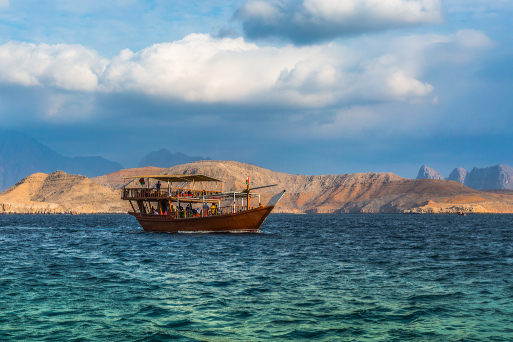Dhow boat Cruise in Arabian Peninsula, boat on blue water with desert mountains in background