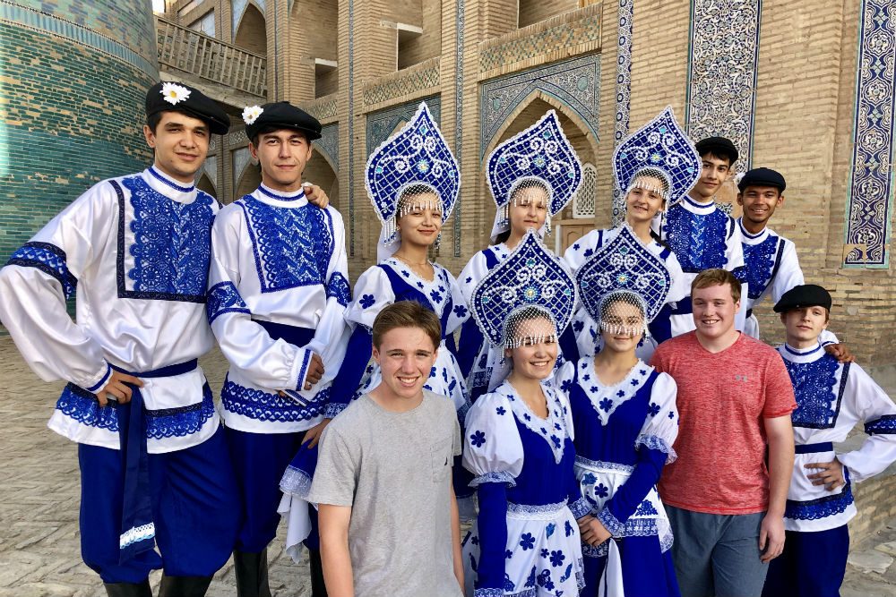 american tourists posing with dancers in traditional blue and white dress in Uzbekistan