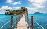 pier walking bridge over turquoise water going to a small island with trees Agios Sostis Greece