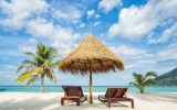palapa with two beach chairs on a beach with turquoise ocean and palm trees