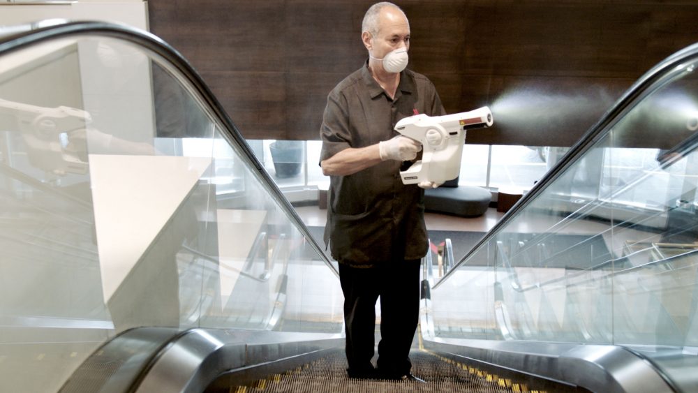 worker using electrostatic sprayer to clean hotel escalator for coronavirus covid safety