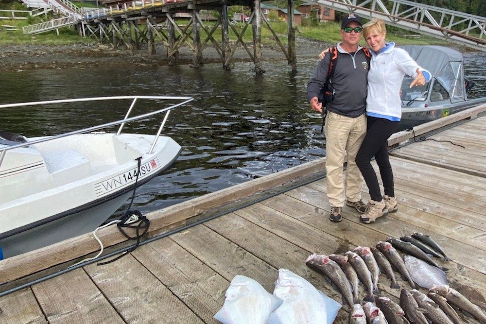 couple on boat dock in alaska posing with fish from fishing trip