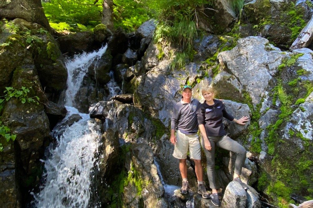 a couple poses in the woods by a waterfall in Alaska