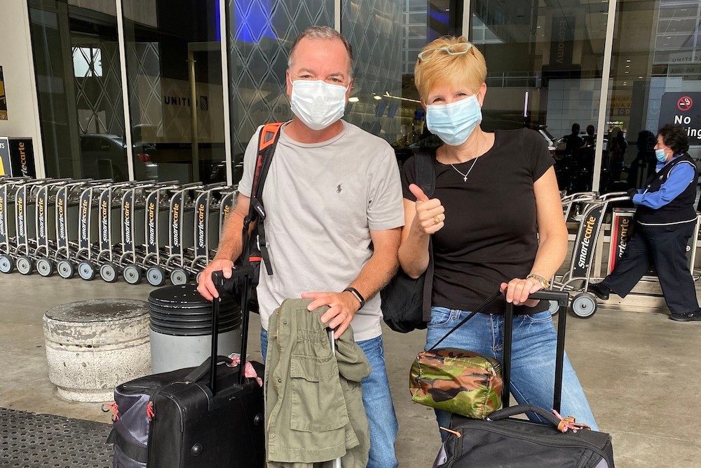 couuple in masks with luggage at airport