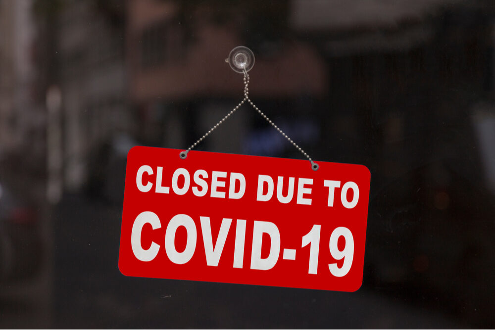 Close-up on a red closed sign in the window of a shop displaying the message "Closed due to Covid-19".