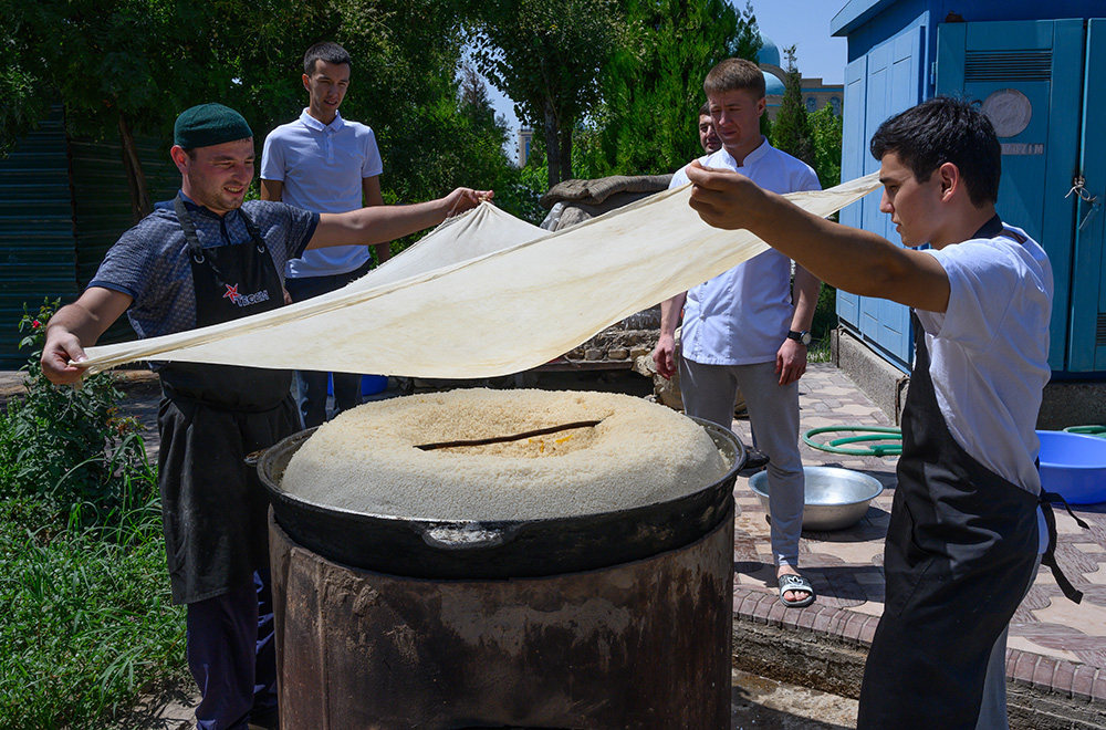 Uzbekistan Men cook a truck tire sized pan of plov over a fire pit 