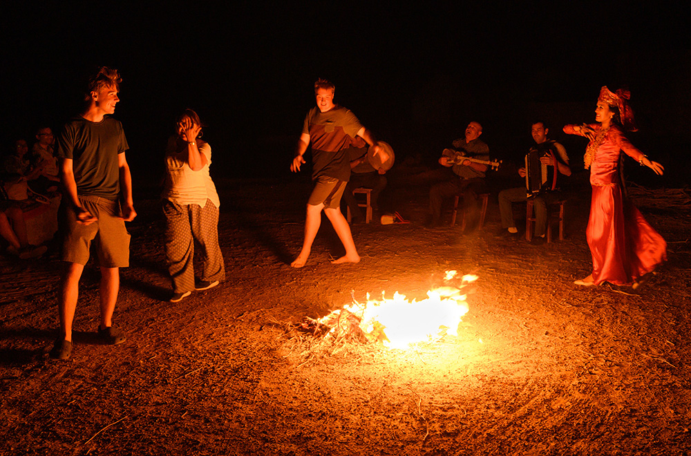 tourists and locals dancing around a campfire at a yurt camp in Uzbekistan