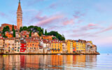 Rovinj Croatia. Sunrise sky above vintage town at Istria peninsula in Adriatic Sea. View from water at old Mediterranean architecture buildings. Coastline and tower of Church of Saint Euphemia.