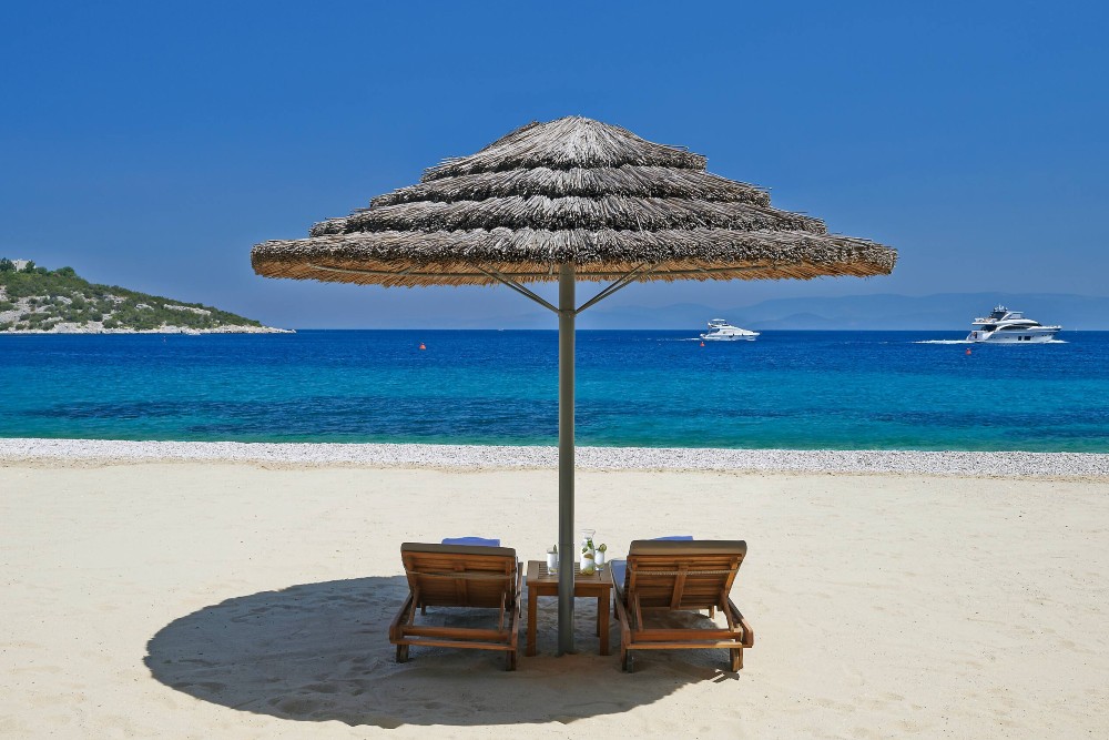 beach lounges under a palapa on the beach looking out to the blue ocean with boats in the water at the Mandarin Oriental hotel Bodrum Turkey