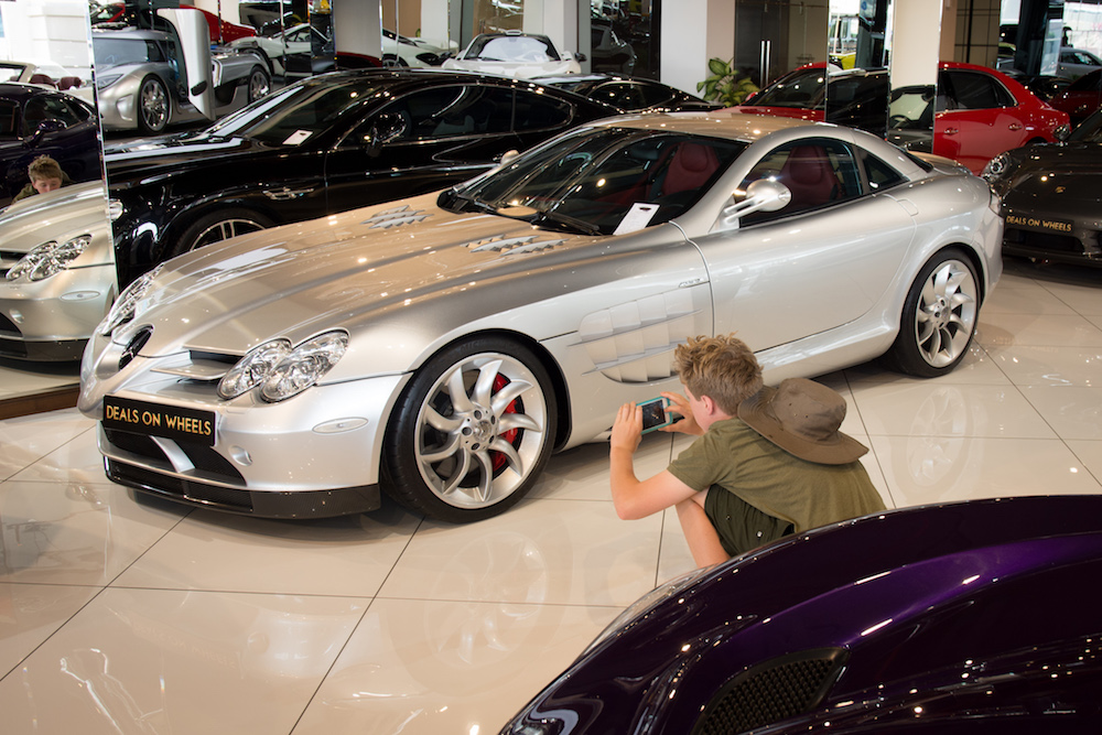 teenage boy taking photos of silver supercar in Dubai at Deals on Wheels auto store