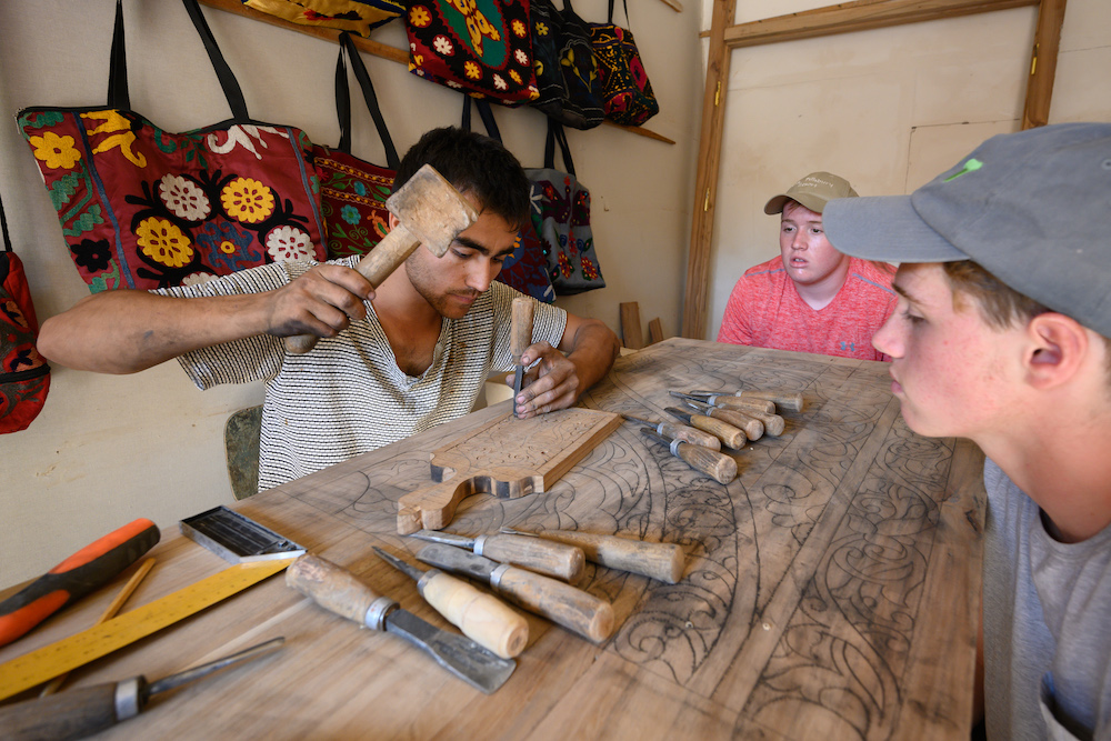 American teenage boy traveler gets woodworking lesson from local craftsman in Khiva Uzbekistan