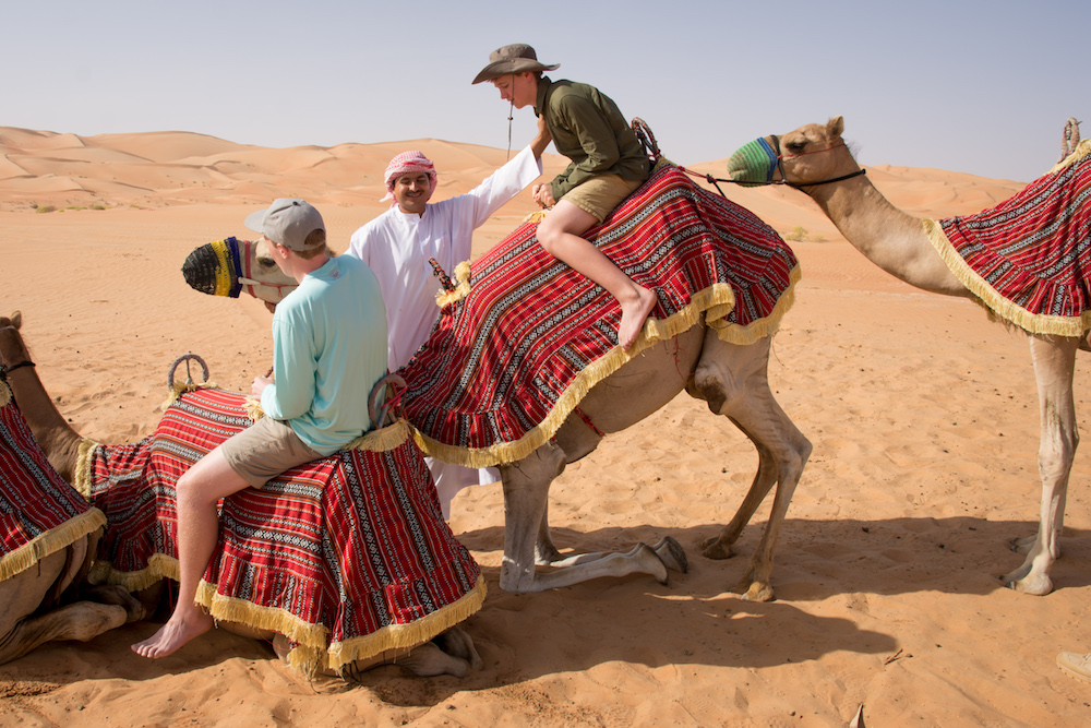 Abu Dhabi teenage boy tourist getting up on camel