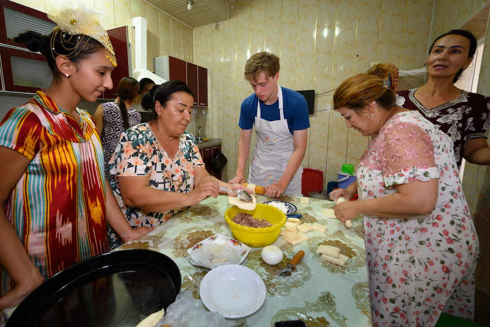 American teenage boy traveler learns how to make baklava in kitchen of local Uzbek woman with other Uzbek women in a kitchen in Bukhara Uzbekistan