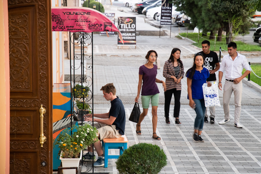 white american teenage boy playing piano on sidewalk in Samarkand Uzbekistan where public pianos are on the sidewalk