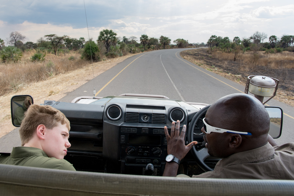 view from a car driving on a road in Zambia, a white tourist boy and an African driver