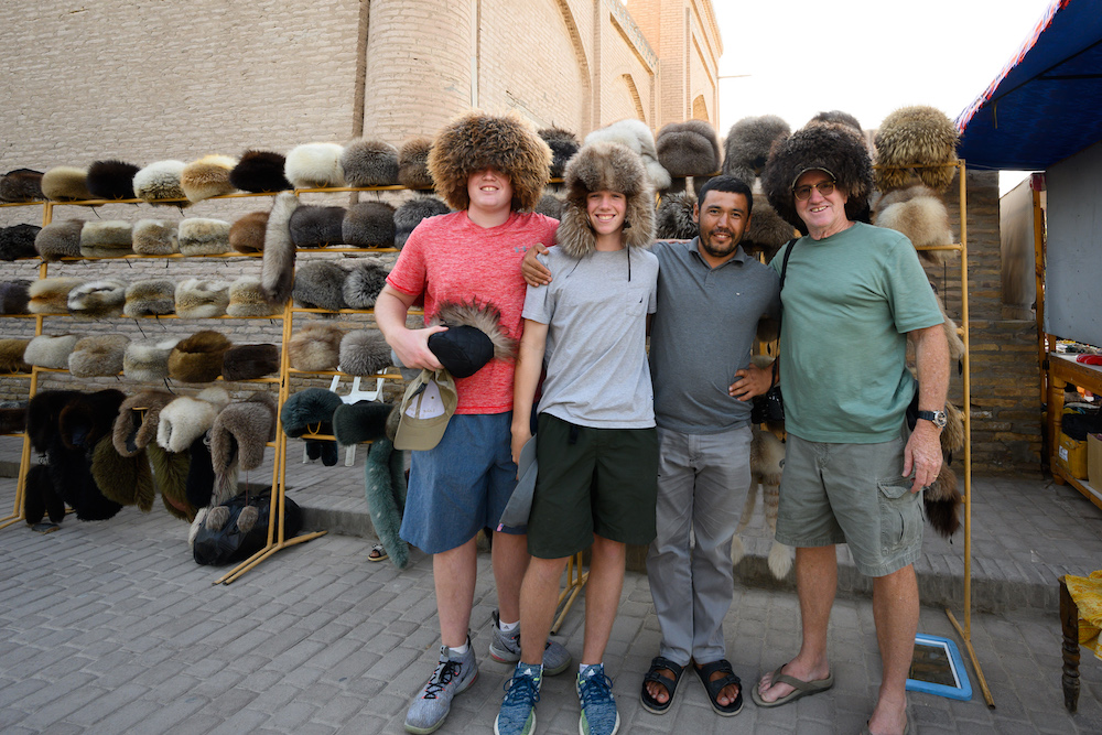 american teenage boy tourists trying on hats at a shop in Uzbekistan and posing smiling with local owner