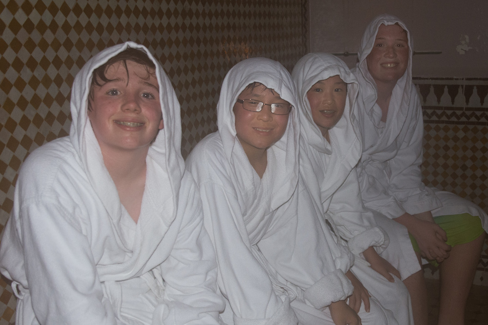 four boys wrapped in robes and towels in a hammam in Morocco