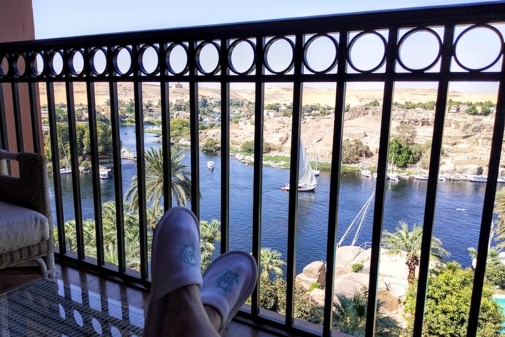 traveler's feet on balcony of Old Cataract Hotel room in Aswan Egypt Overlooking the Nile and elephantine island