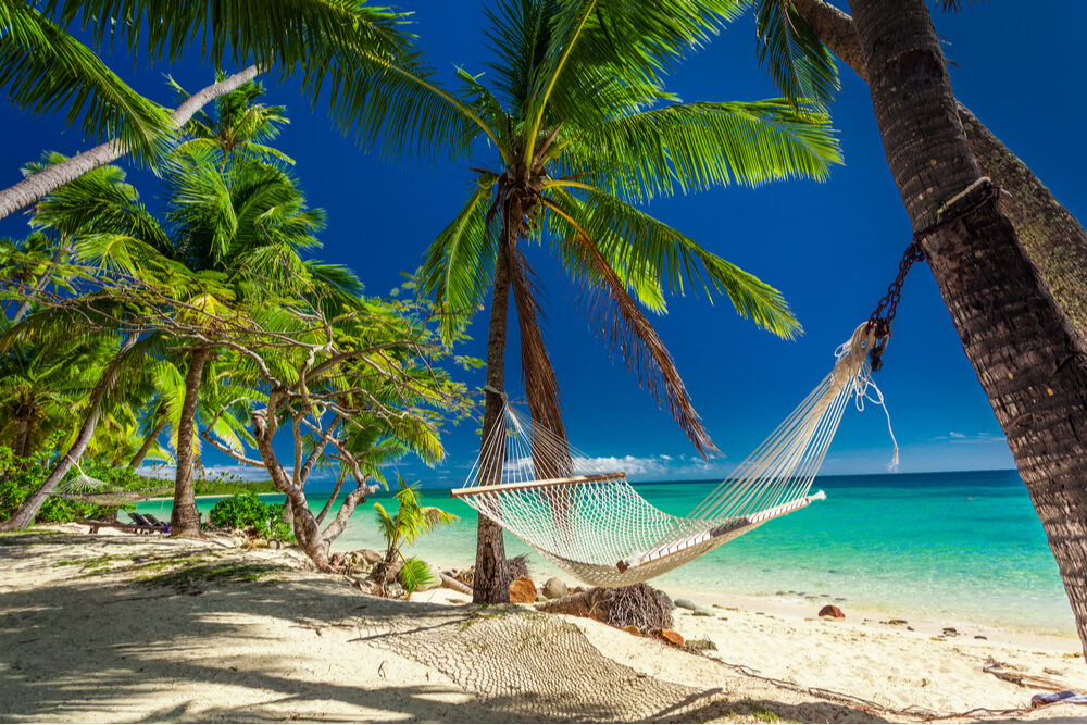 hammock between palm trees on a beach in Fiji with turquoise ocean in background