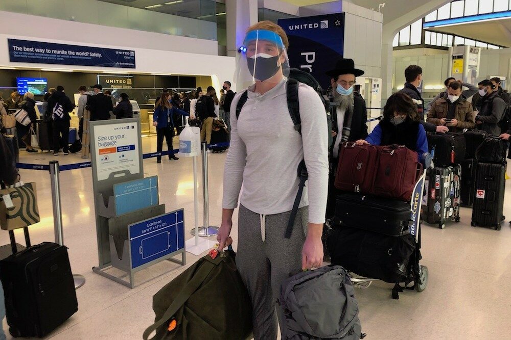 teenage boy check-in line at airport with masks and face shield covid era pandemic