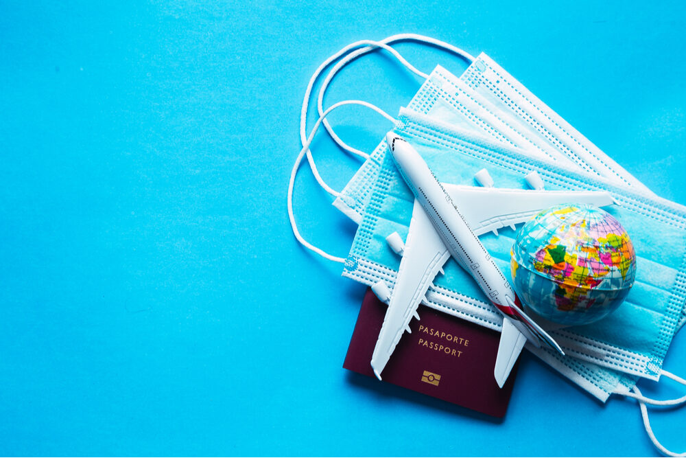 stock photo of toy airplane on stack of masks and passport with a globe signifying travel during Covid