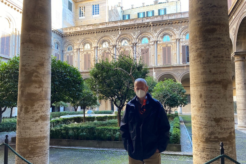 older male traveler wearing mask standing in front of Doria Pamphilj Palace Rome Italy