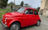 older male traveler in a red vintage Fiat car touring ruins around Rome Italy