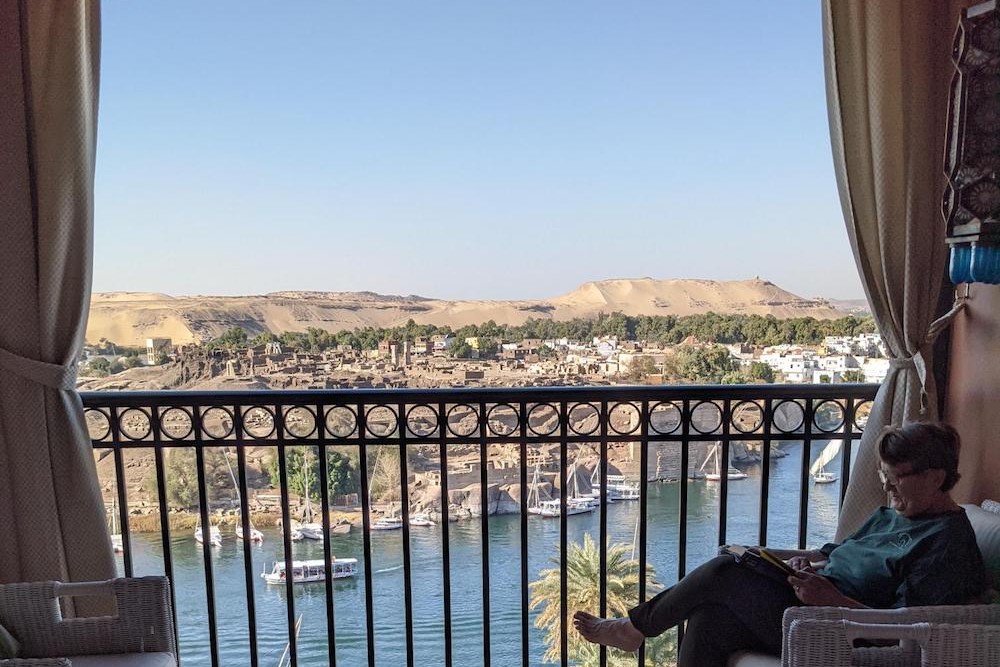 view of the Nile and Elephantine island from Old Cataract hotel balcony with tourist woman reading magazine on balcony Aswan Egypt