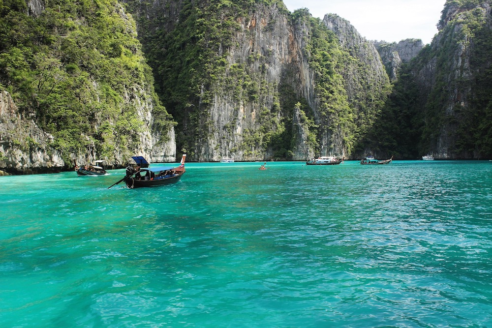 boats on turquoise water of Ko Phi Phi Le with limestone cliffs coming out of the water in Thailand