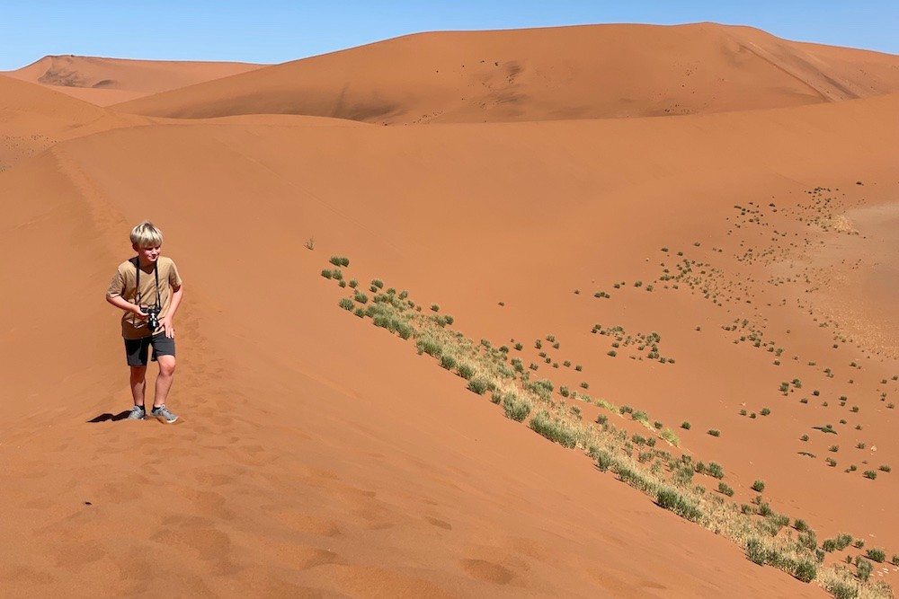 young blond tourist boy walking in Namibia desert with camera