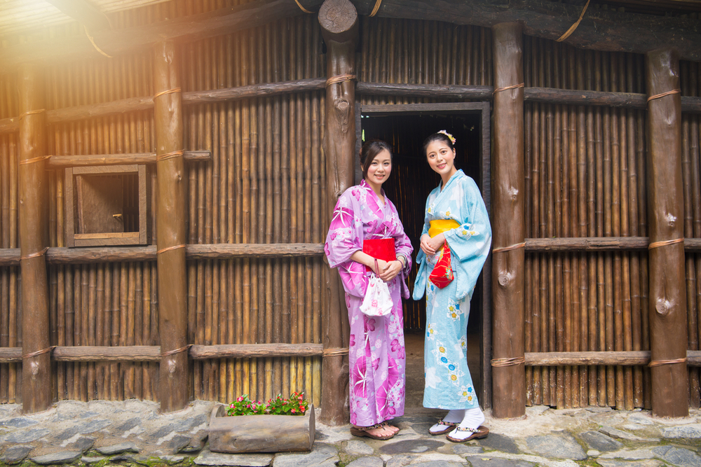 Elegant female travelers wearing traditional clothing dress kimono standing in front of old wooden house door outside.