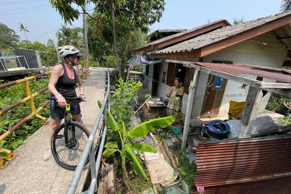 Brook on a bike and a local woman outside her home in Bangkok