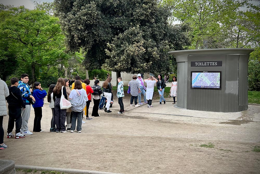 A long line of people in Champ de Mars waiting in front of the public toilets.