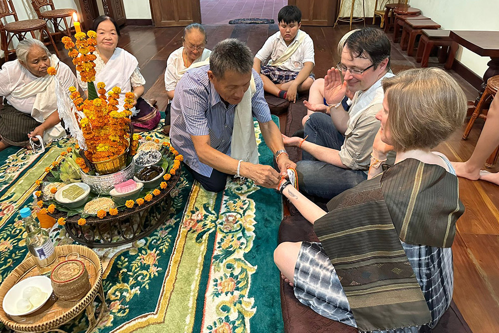 A man tying string around Brook's wrist as a part of the Baci ceremony.